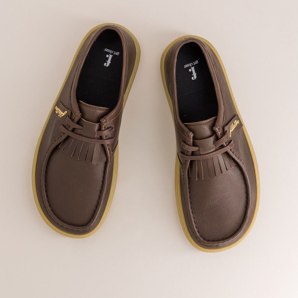 Pair of brown barefoot derbies with yellow soles on a light beige background