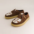 Pair of brown barefoot derbies with white and brown cow print soles on a light gray background
