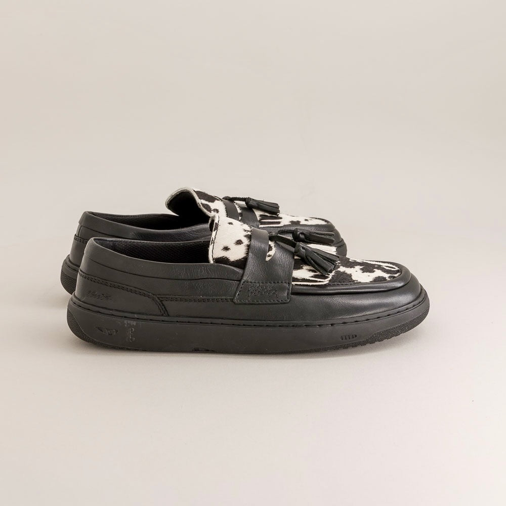 Black slip-on shoes with cow print accents on a light gray background