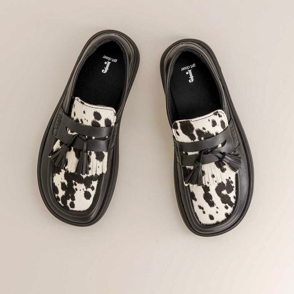 Pair of black and white cow print barefoot loafers on a light gray background