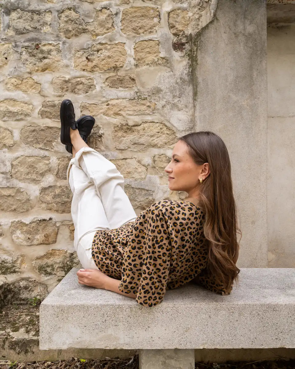 Woman in leopard print outfit sitting on a stone bench against a stone wall.