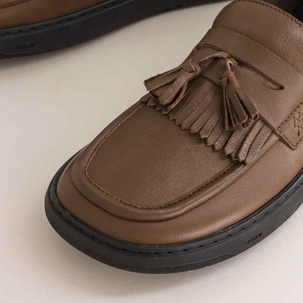 Brown barefoot loafer shoe with tassels on a light background