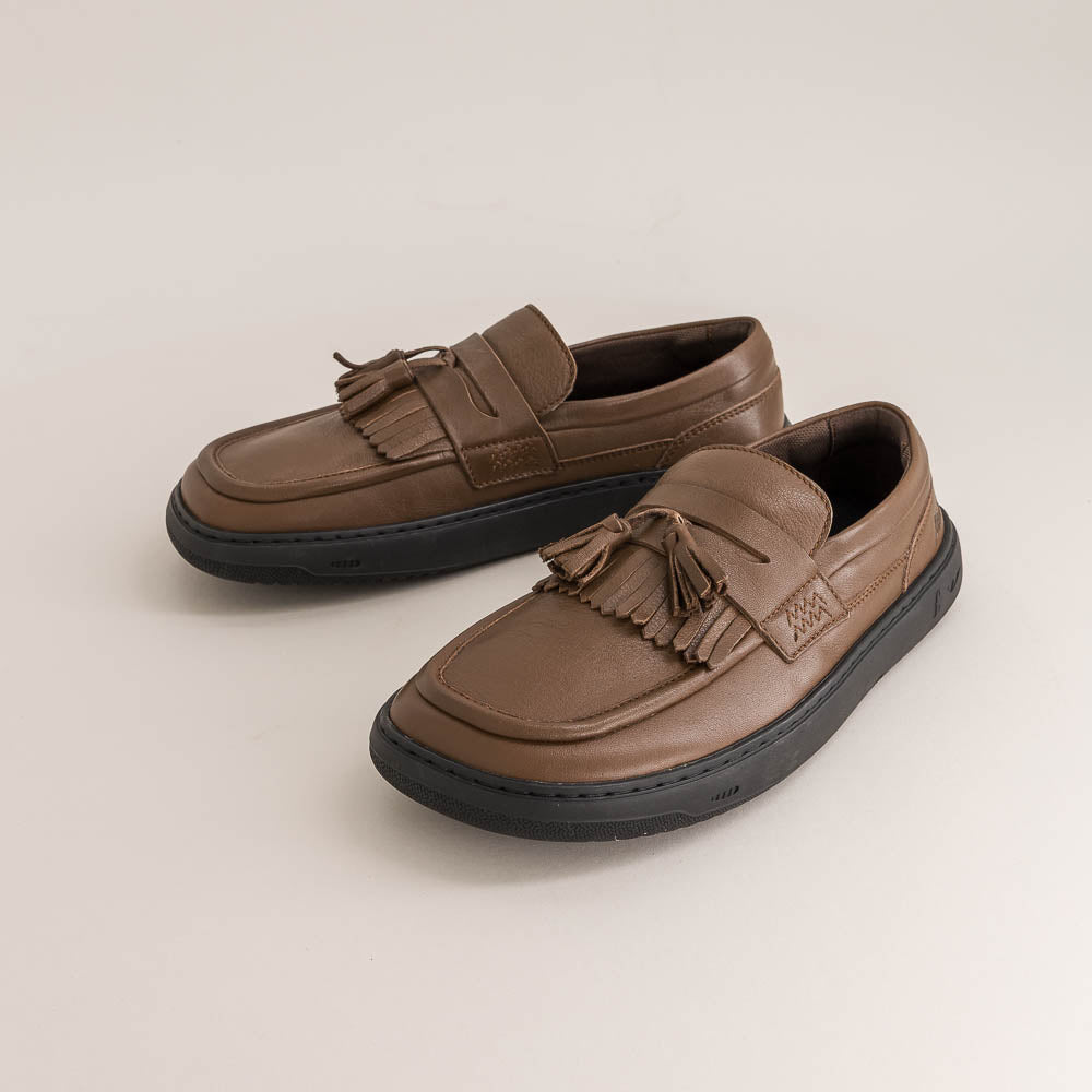 Pair of brown barefoot loafers with tassels on a beige background