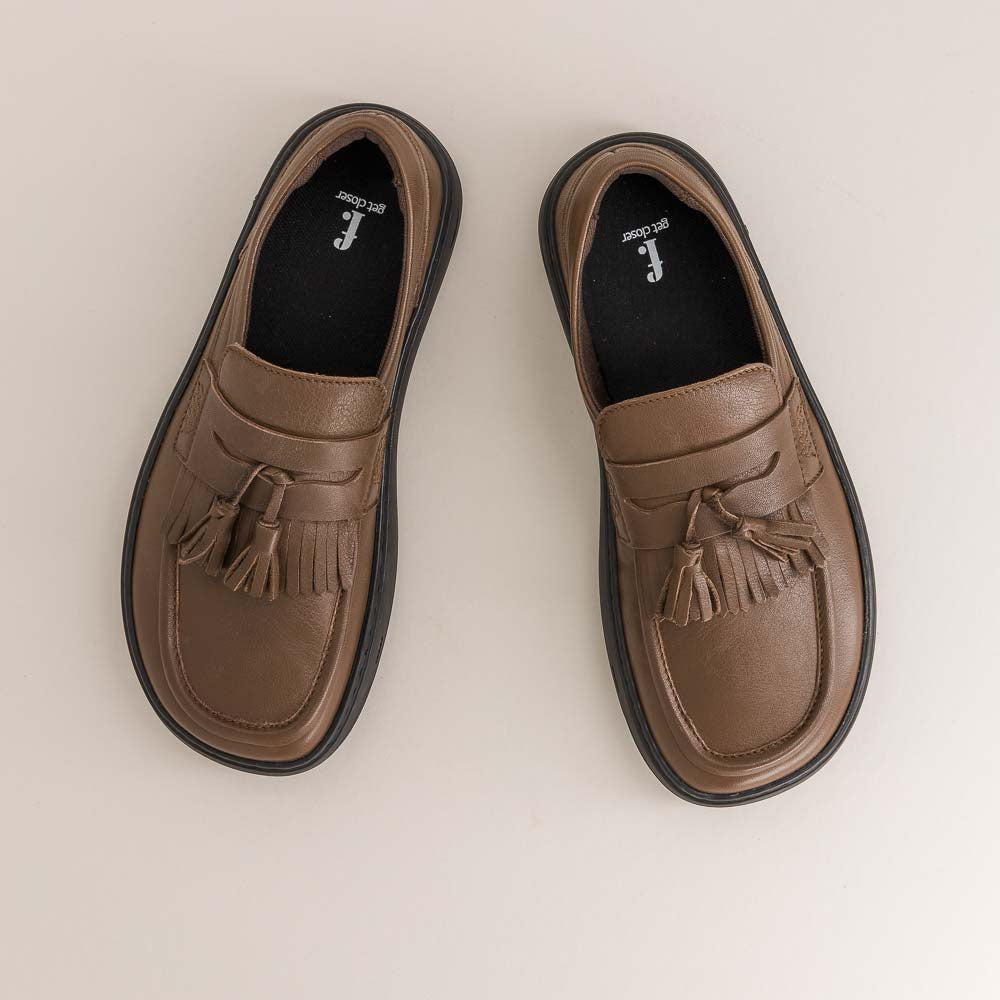 Pair of brown barefoot loafers with tassels on a beige background