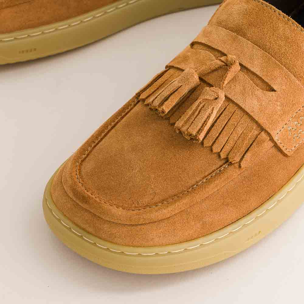 Tan suede loafer with tassel on a light background