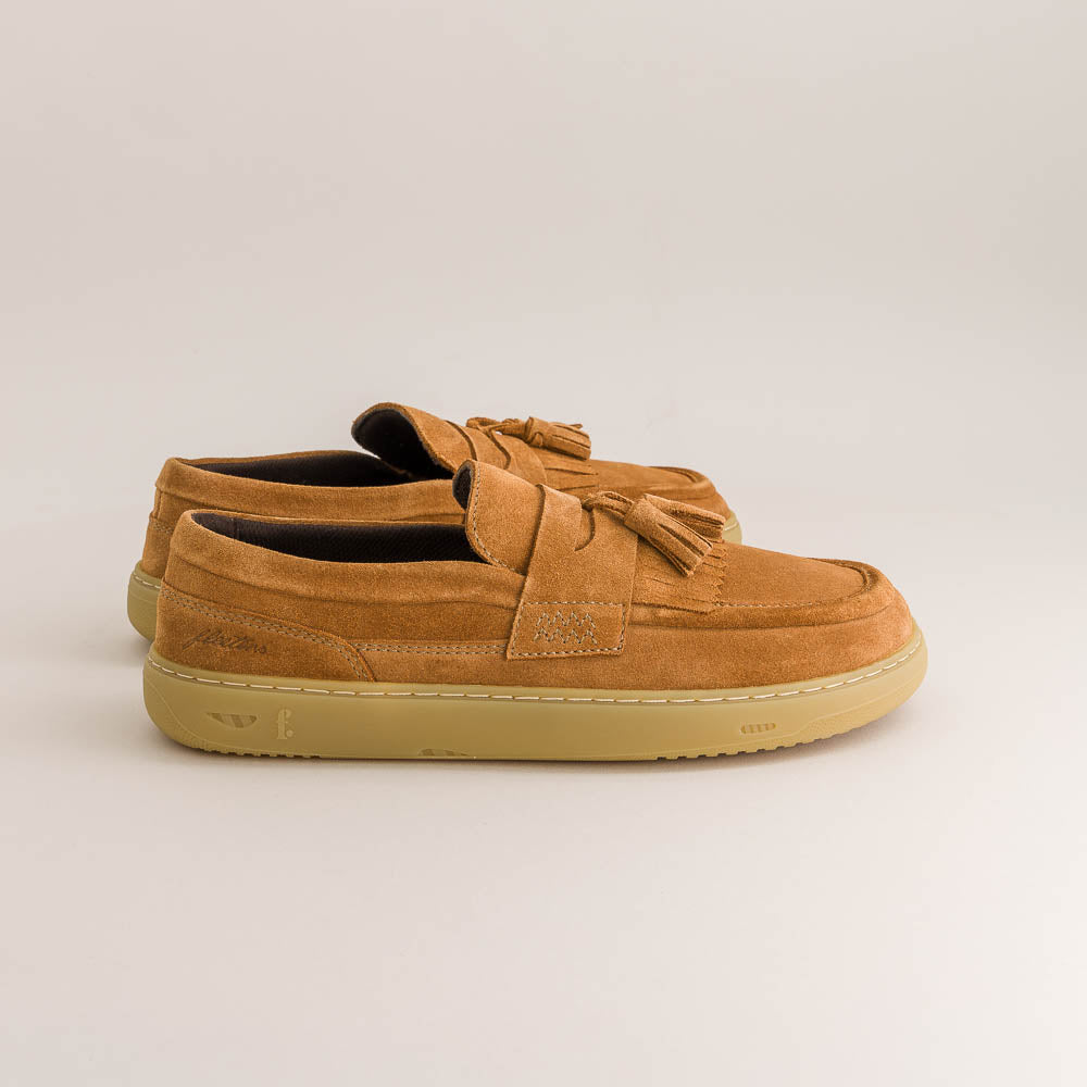 Pair of tan suede shoes with tassels on a light beige background