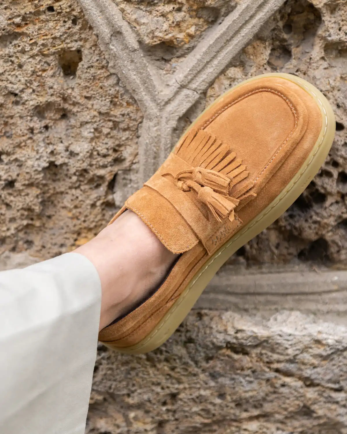 Tan suede barefoot loafer with tassel on a stone surface