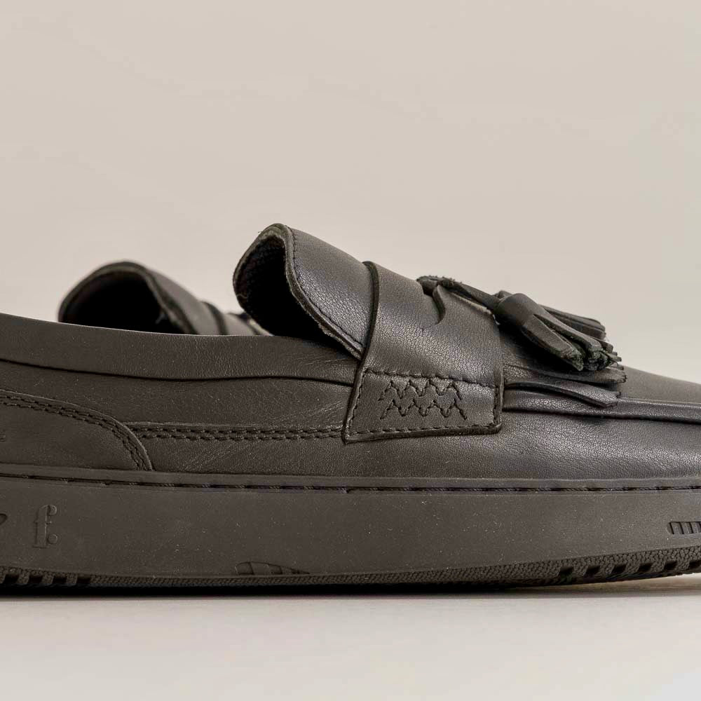 Black loafers with tassels on a light gray background