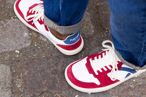 Red and white barefoot sneakers with blue accents on a pavement