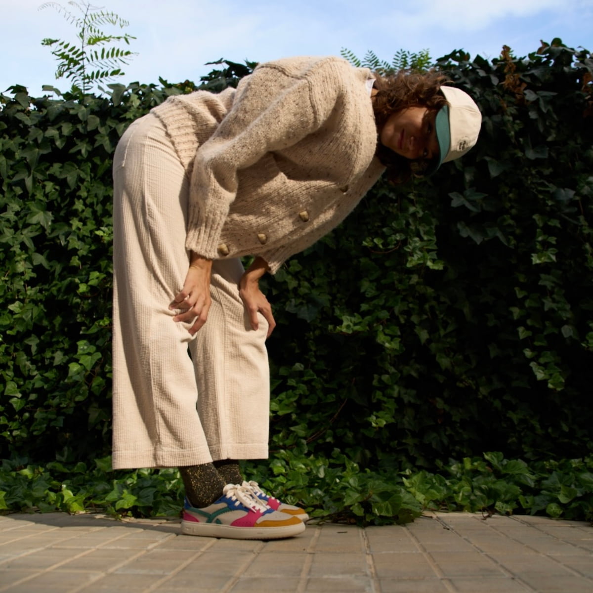 Person wearing a  multicolored barefoot sneaker with greenery in the background.