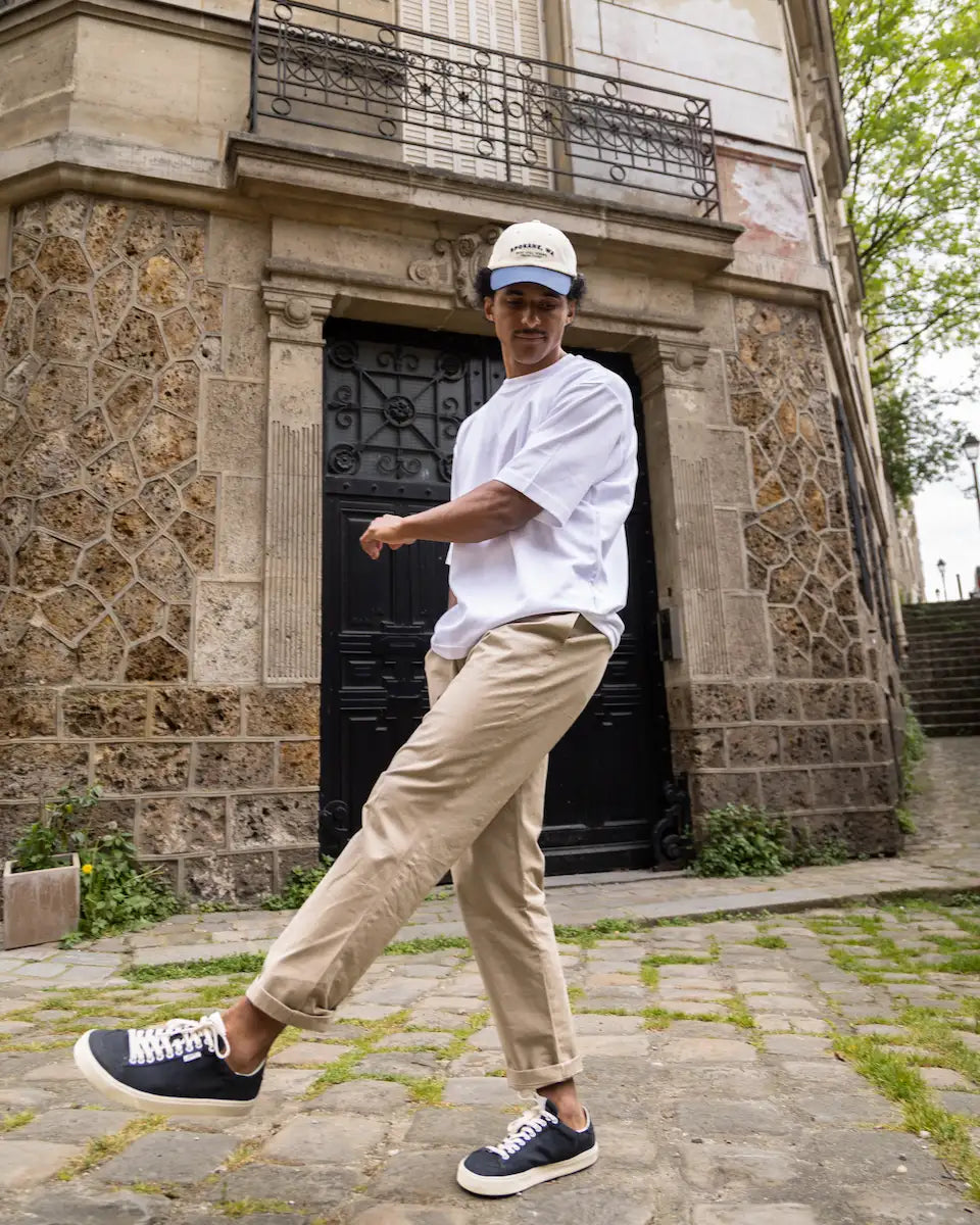 Person in white shirt and beige pants dancing in front of a stone building.