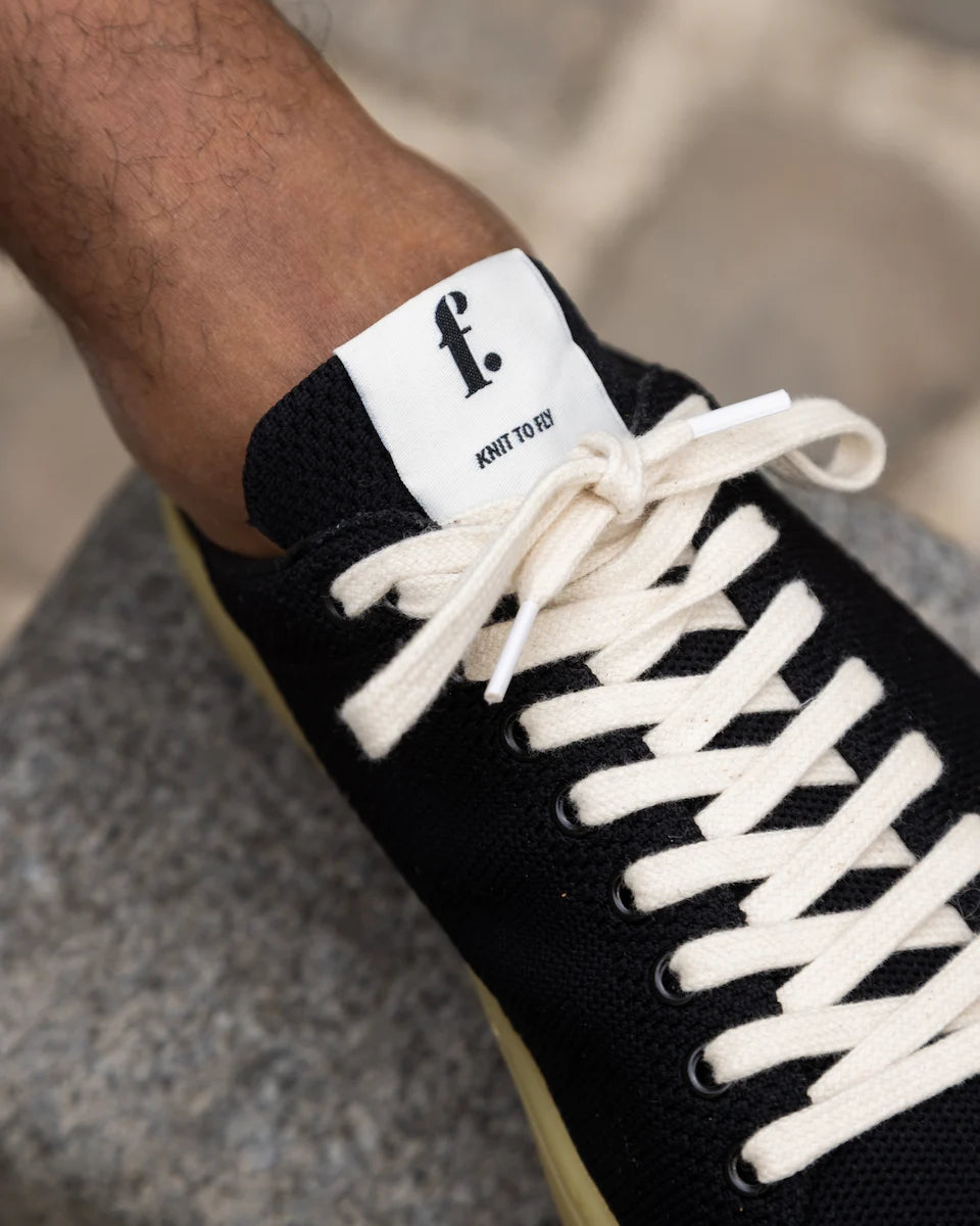 Black knit barefoot sneaker with white laces and a visible brand logo on a blurred background