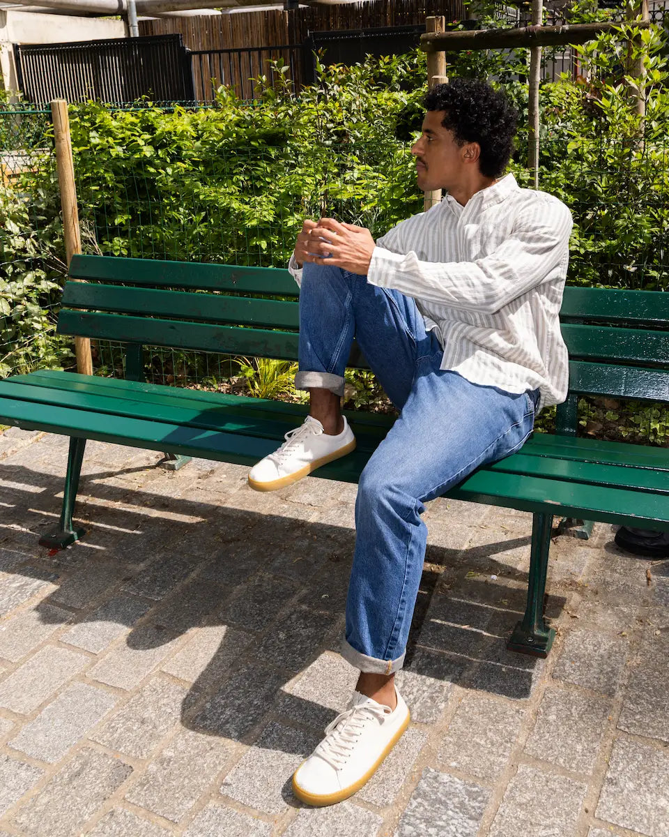 Man sitting on a green bench in an outdoor setting wearing knit barefoot sneakers.