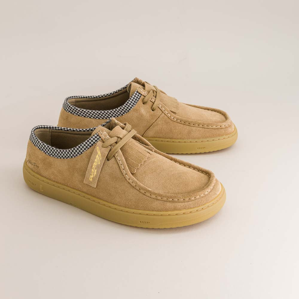Pair of tan barefoot derbies with checkered lining on a beige background