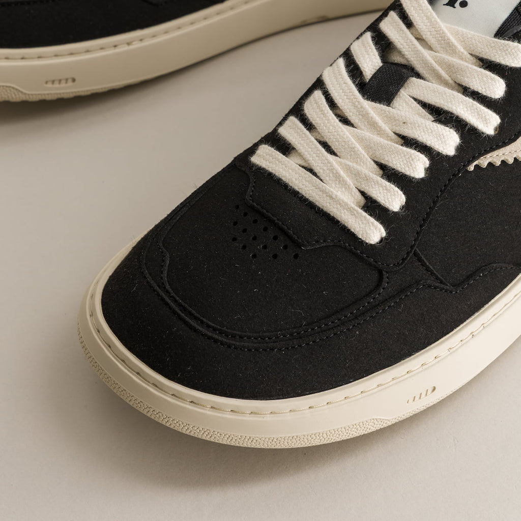 Black sneaker with white laces on a light gray background