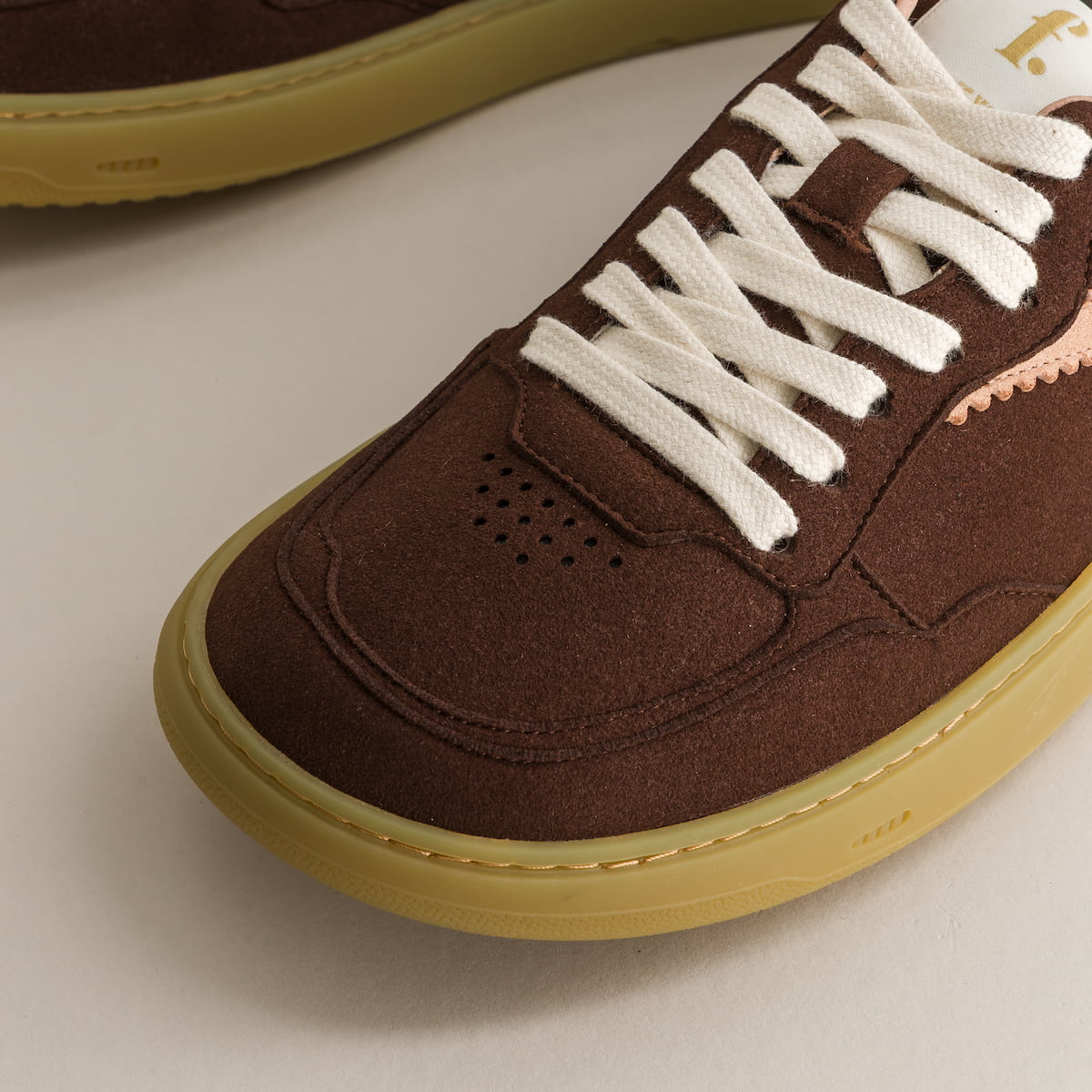 Brown sneaker with white laces on a beige background