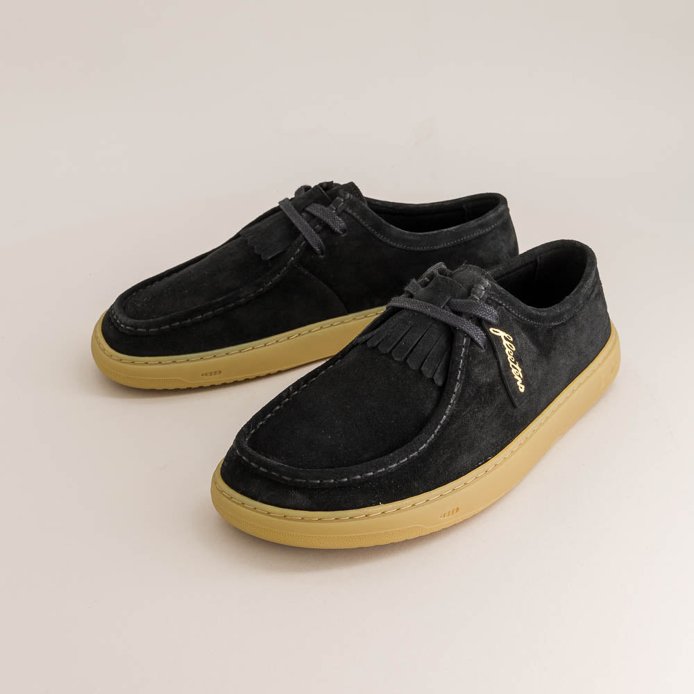 Pair of black suede shoes with tan soles on a light beige background