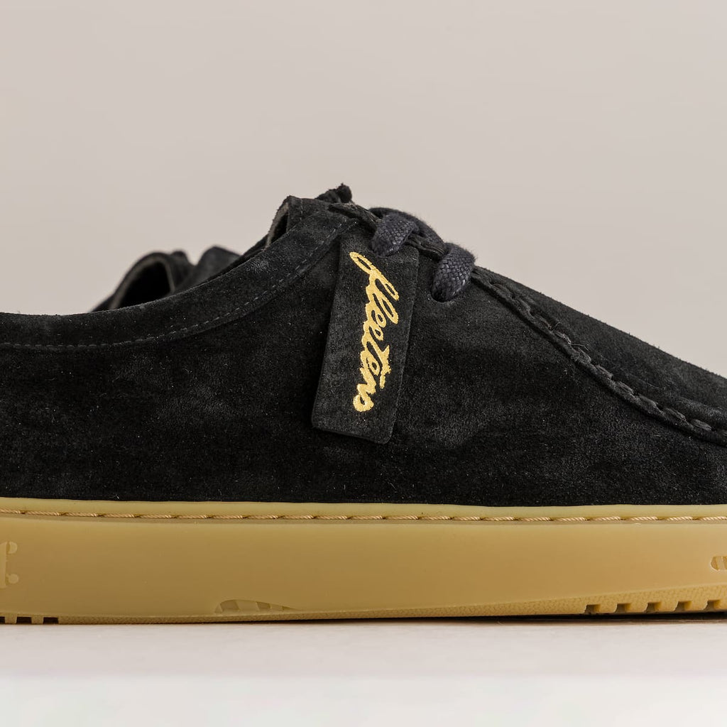 Black sneaker with gold sole and brand logo on a beige background