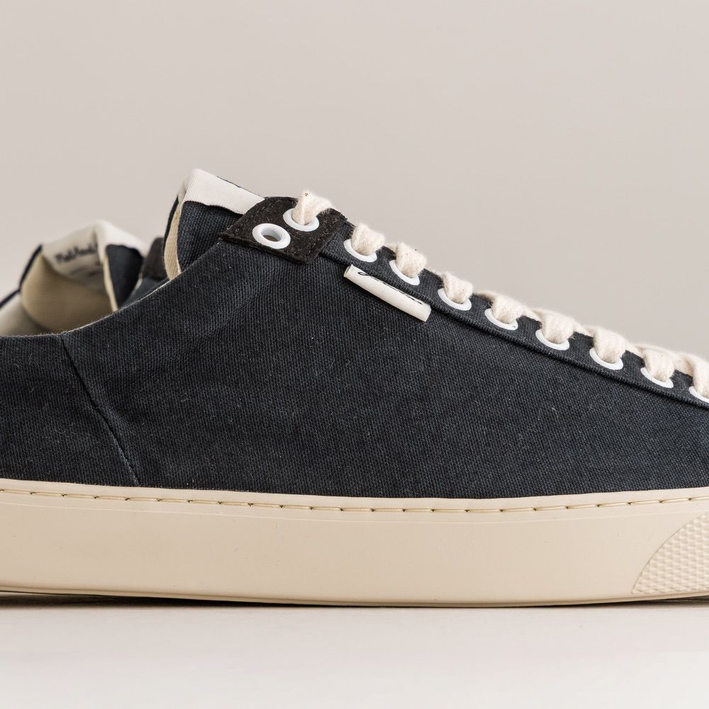 Black sneaker with white laces and sole on a light gray background