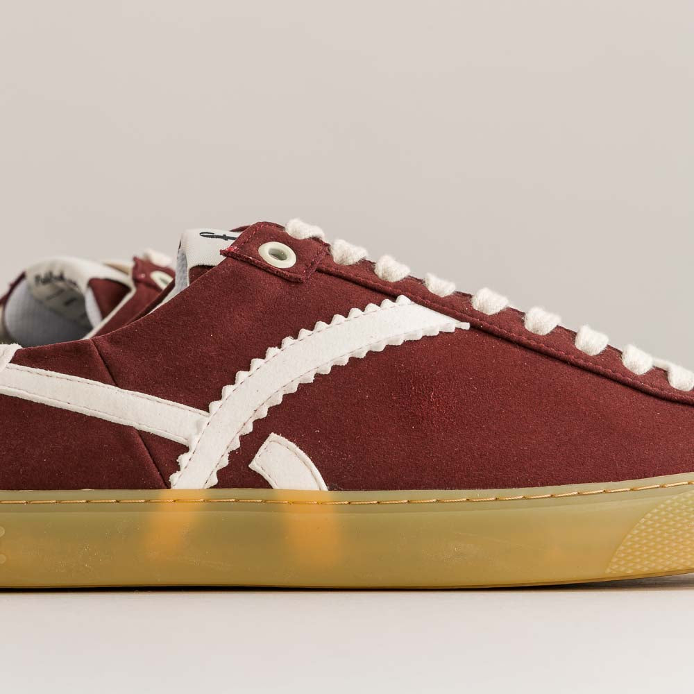 Maroon sneaker with white laces and gold sole on a gray background