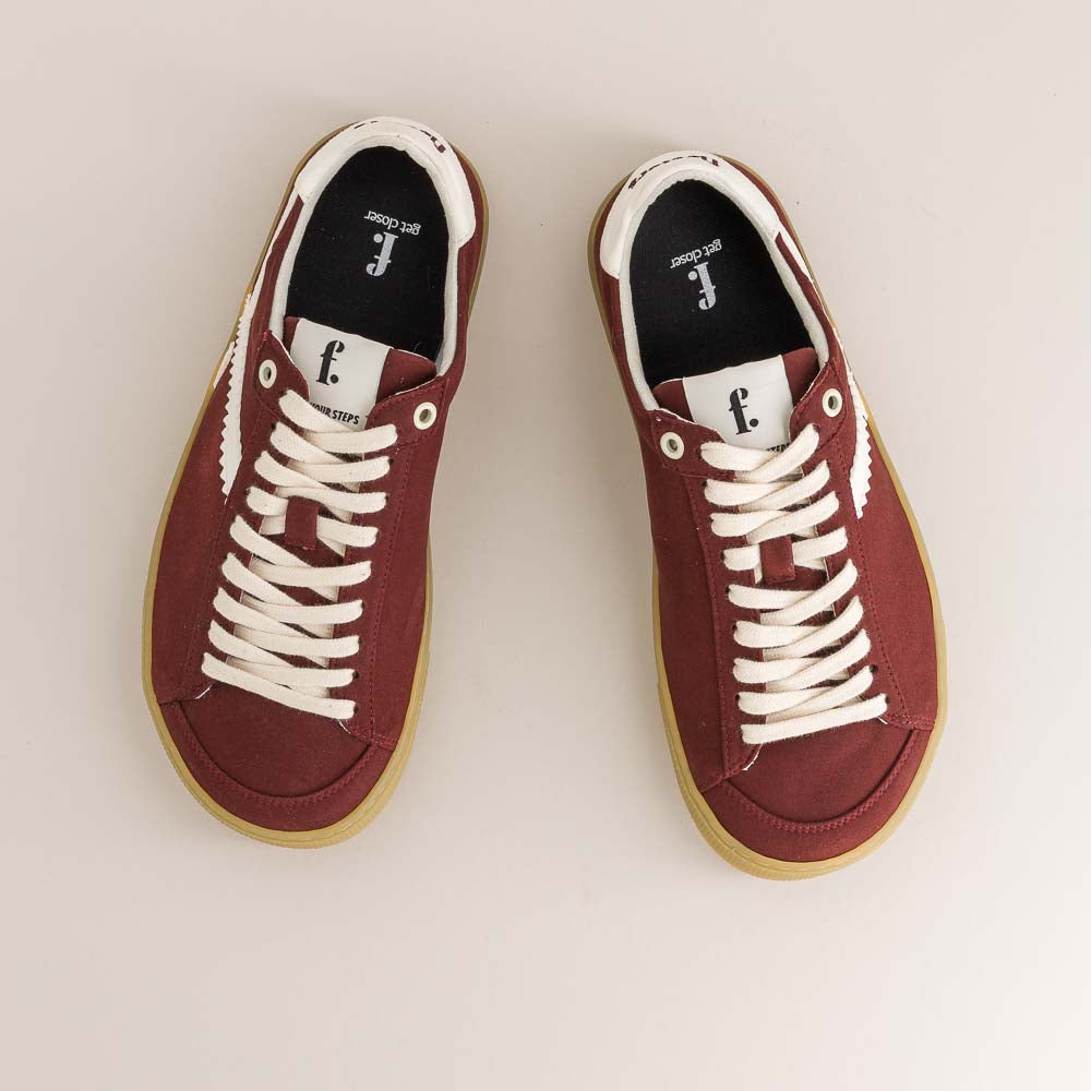 Pair of maroon barefoot sneakers with white laces on a beige background