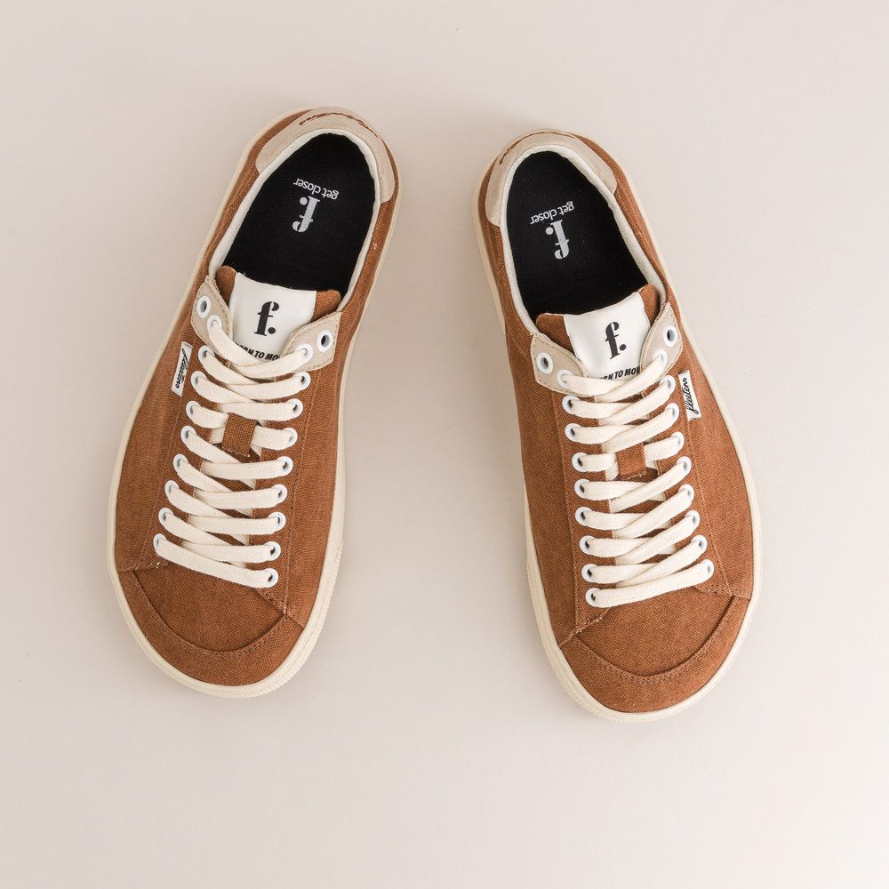 Pair of brown minimalist sneakers with white laces on a light background