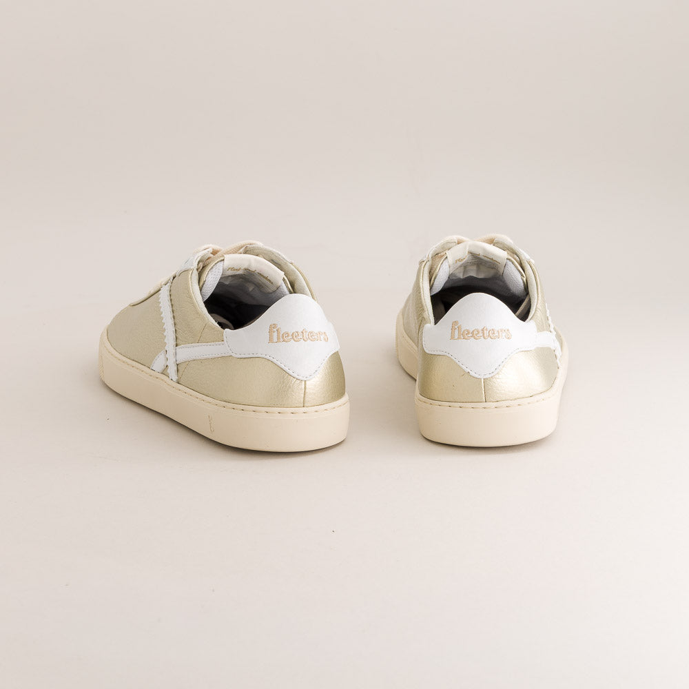 Pair of gold sneakers with white soles on a beige background