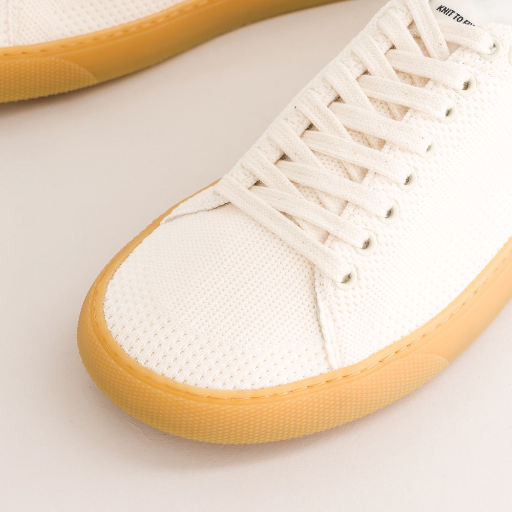 Close-up of a white knit barefoot sneaker with yellow sole on a light background