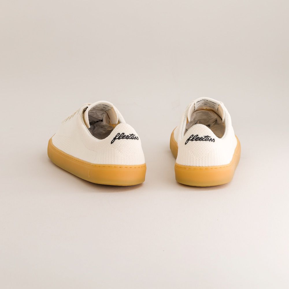 Pair of white knit barefoot sneakers with yellow soles on a light gray background