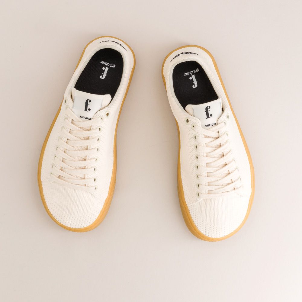 Pair of white knit barefoot sneakers with yellow soles on a light gray background