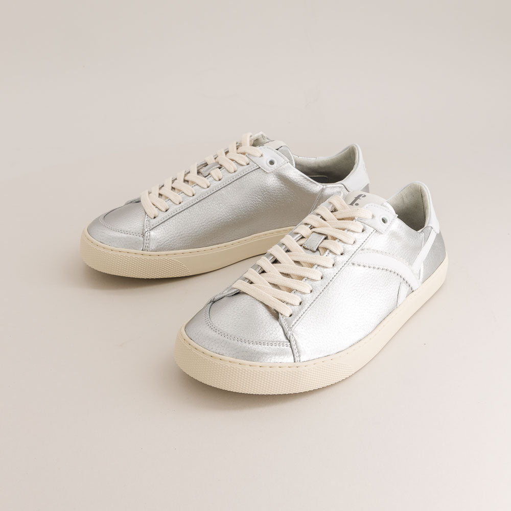 Pair of silver barefoot sneakers with white laces on a beige background