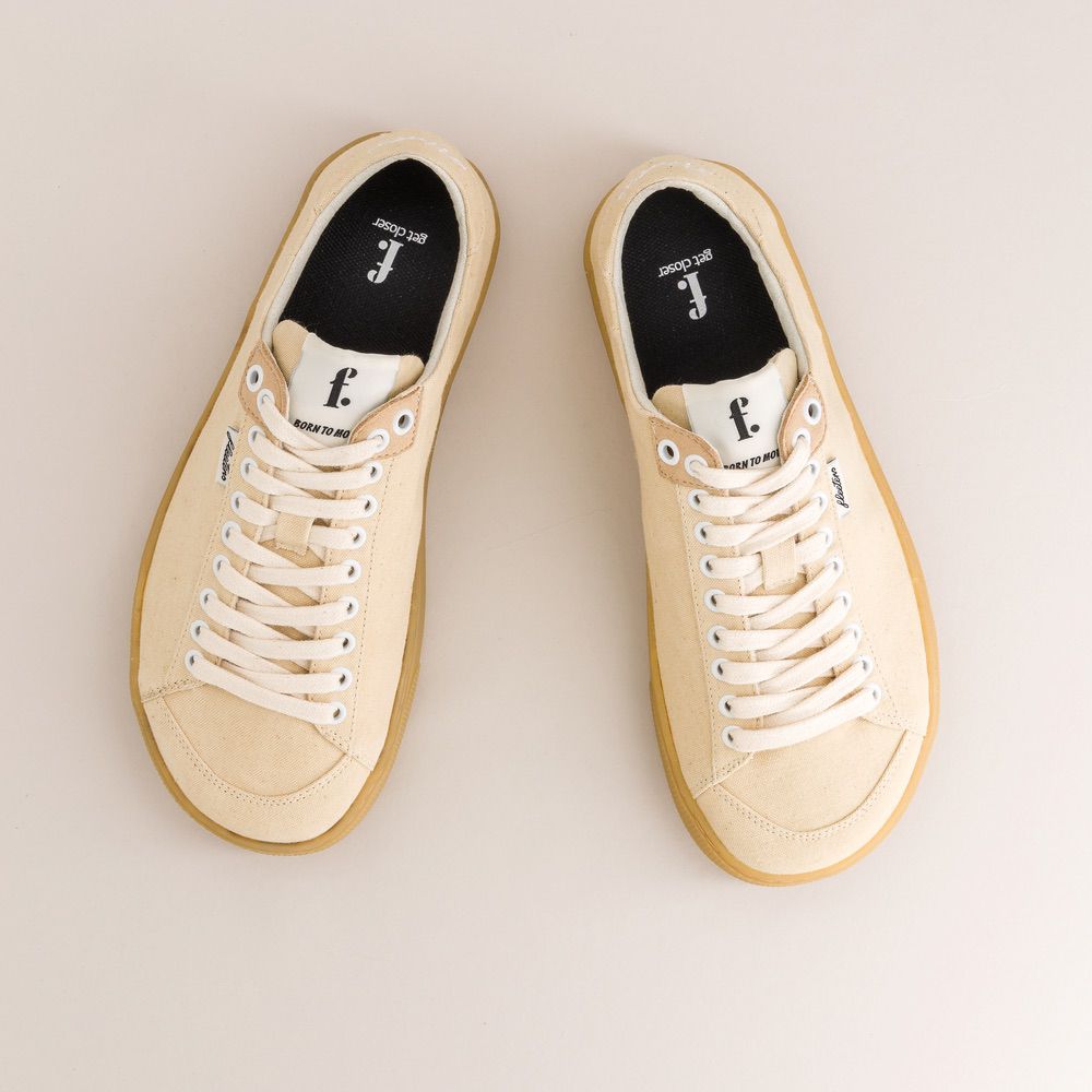 Pair of beige canvas sneakers with white laces on a light background