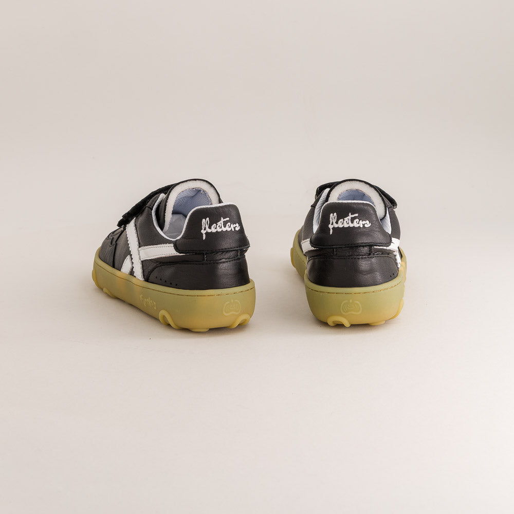 A pair of black leather low-top sneakers with white side stripes and gum soles, shown from the back on a light beige studio background. The brand name 'floretos' is visible in white script on the heel of each shoe.