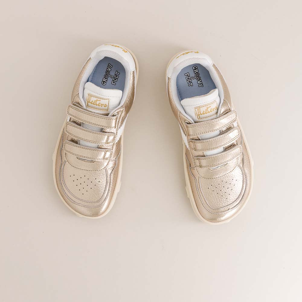 Pair of gold kids barefoot sneakers on a beige background