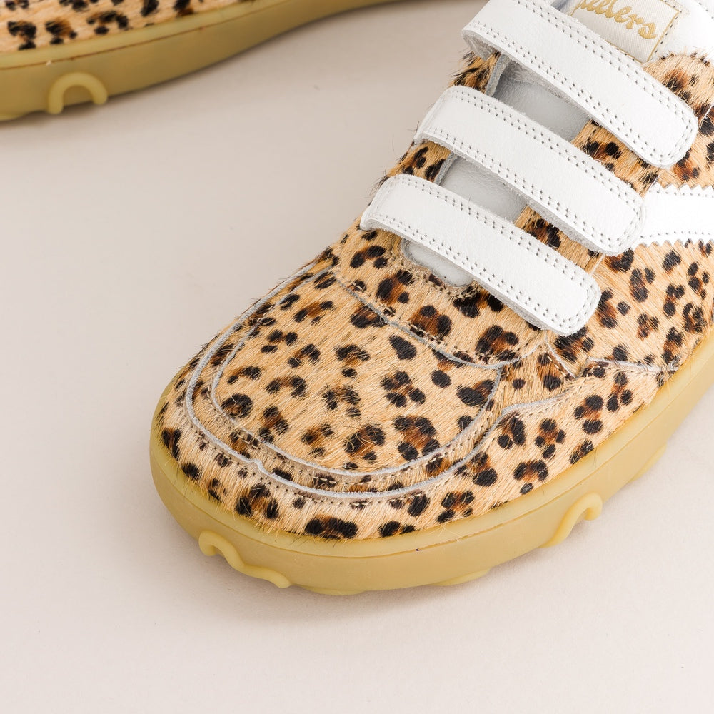 A close-up of a children's barefoot sneaker featuring a beige and brown leopard print upper, white hook-and-loop strap closures, and a light yellow sole.