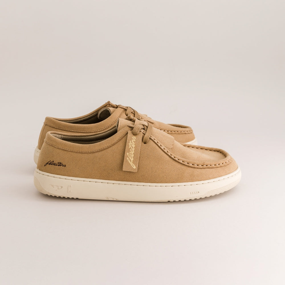 A pair of tan suede boat shoes with off-white rubber soles, shown from a side profile view on a light gray background.