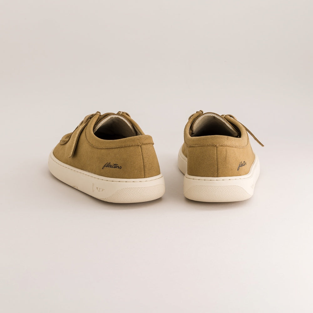 A pair of low-top derbies shown from the back, featuring a warm tan upper and a thick cream-colored sole, set against a plain light gray background.