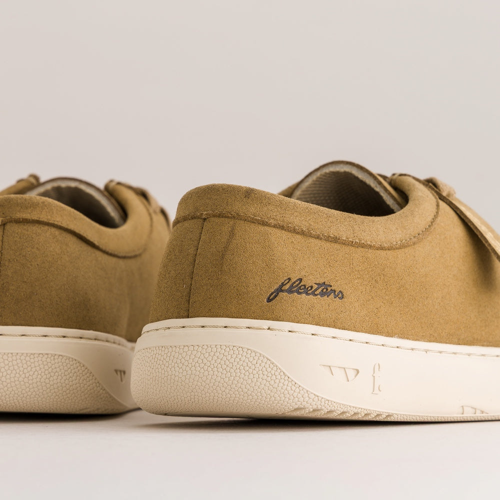 Close-up rear view of tan suede derbies with off-white textured soles and a visible 'fleeters' logo on the heel, photographed on a clean light gray studio background.