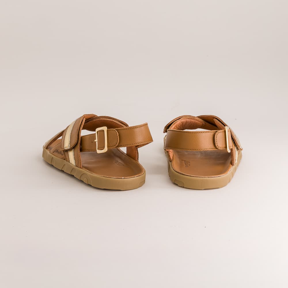 A pair of tan leather slide sandals with adjustable straps and gold-tone buckles, shown from the side against a light gray background.