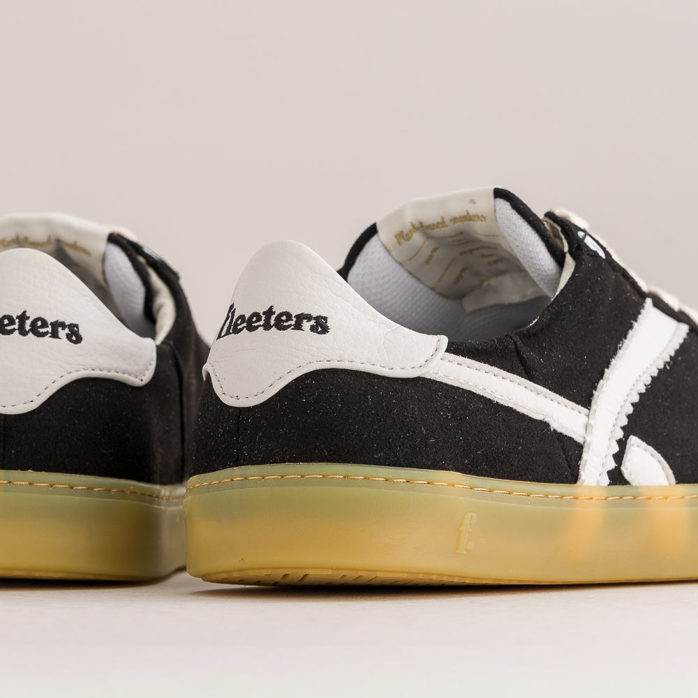 Close-up of a pair of black and white barefoot sneakers showing the heel and side panels, with a translucent gum sole.