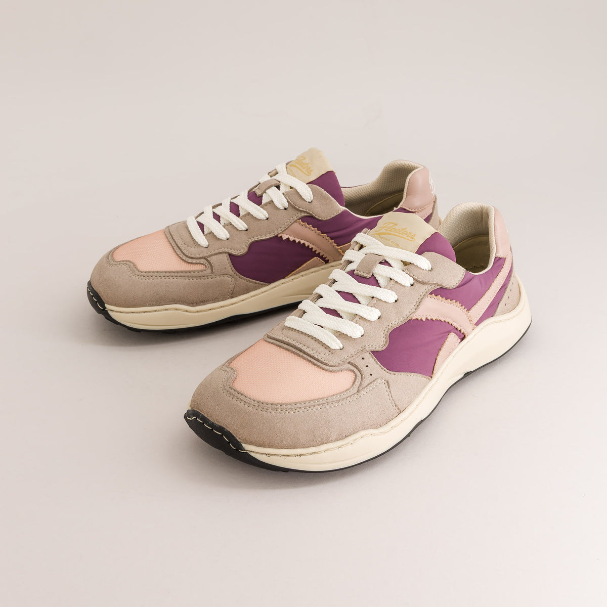 A pair of retro-style low-top barefoot sneakers in beige suede and light pink leather with purple side panels and white laces, photographed on a clean light gray studio background.