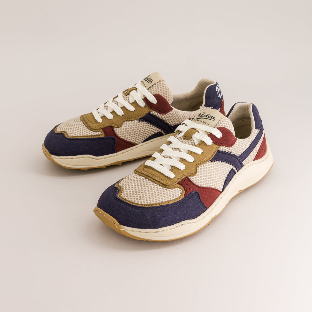 A pair of multicolor retro-style barefoot sneakers with beige mesh, navy blue panels, tan suede overlays, burgundy accents, and white laces, displayed on a light gray studio background.