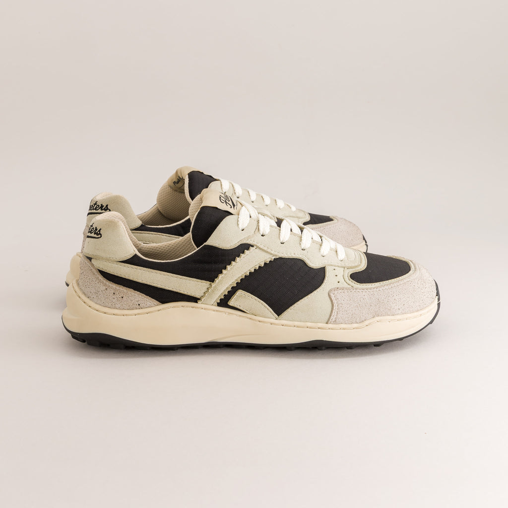 A pair of vintage-style platform barefoot sneakers in cream, black, and light gray suede, shown from a side profile against a neutral light gray background.