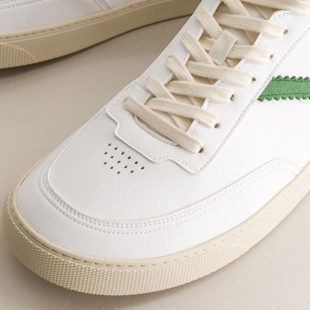 Close-up of a white mid-ankle barefoot sneaker with beige laces on a neutral background