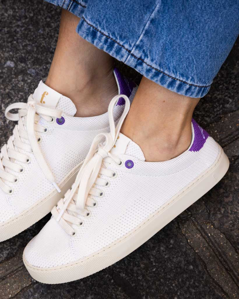 White knit barefoot sneakers with purple accents worn by a person on a dark surface