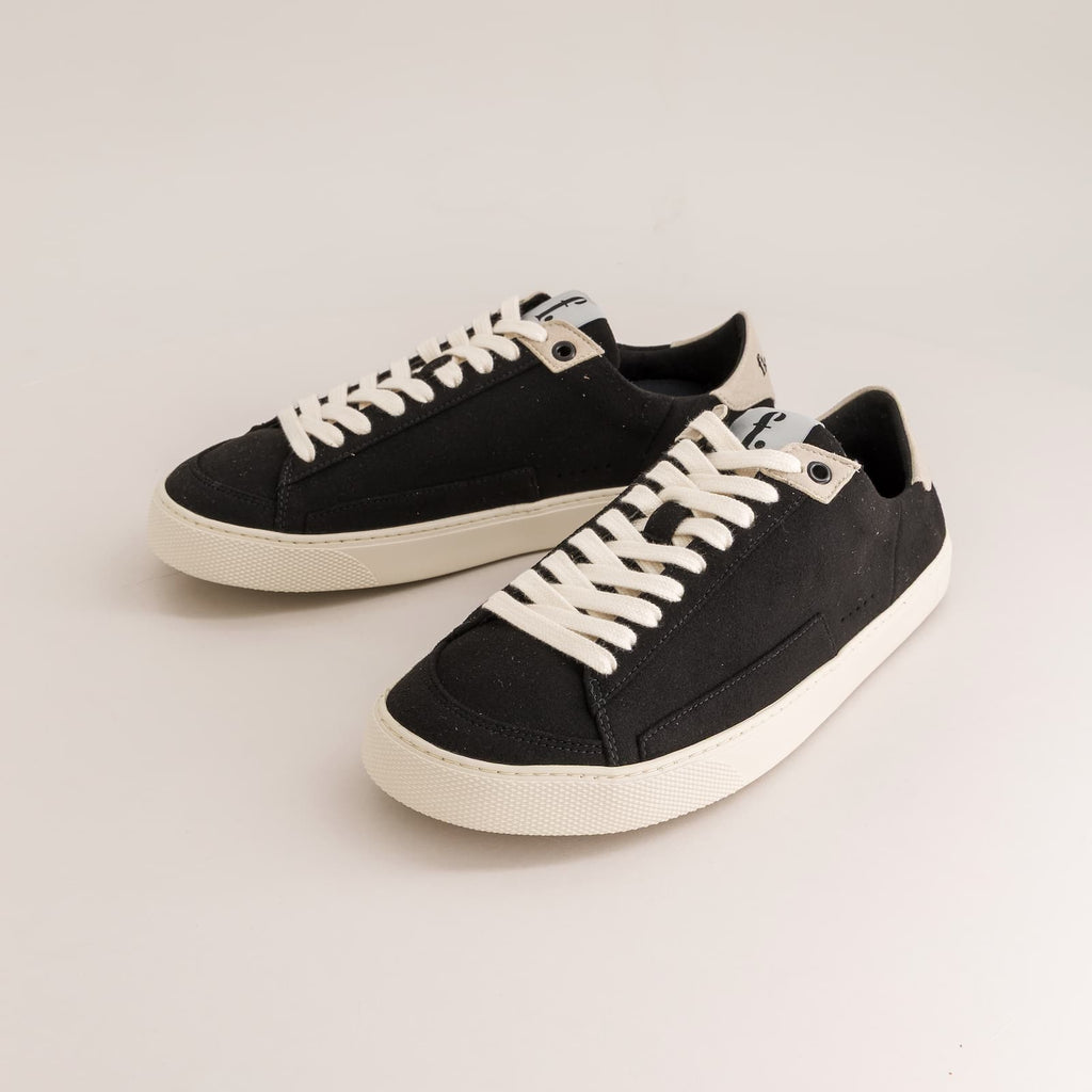 A pair of black canvas low-top barefoot sneakers with off-white laces and off-white rubber soles, displayed on a clean light gray studio background.