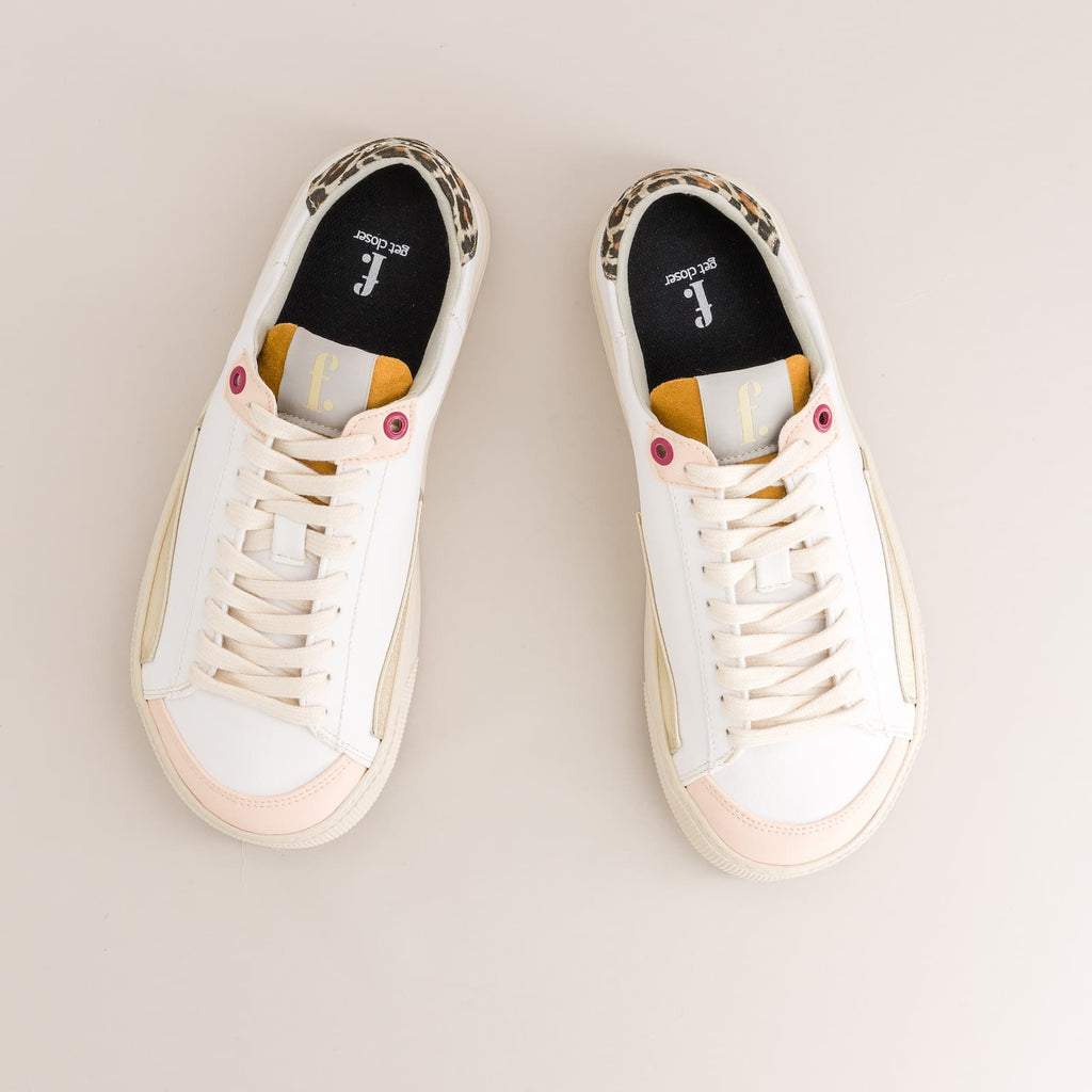 A pair of low-top barefoot sneakers shown from a top-down view on a light beige background. The shoes are primarily white with a pale pink toe cap, cream laces, a leopard print heel tab, and yellow accents on the collar lining and inner sole.