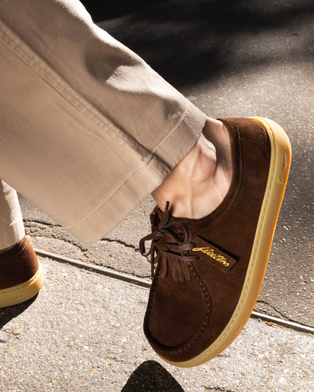 Brown suede shoes with a brand logo on a concrete surface