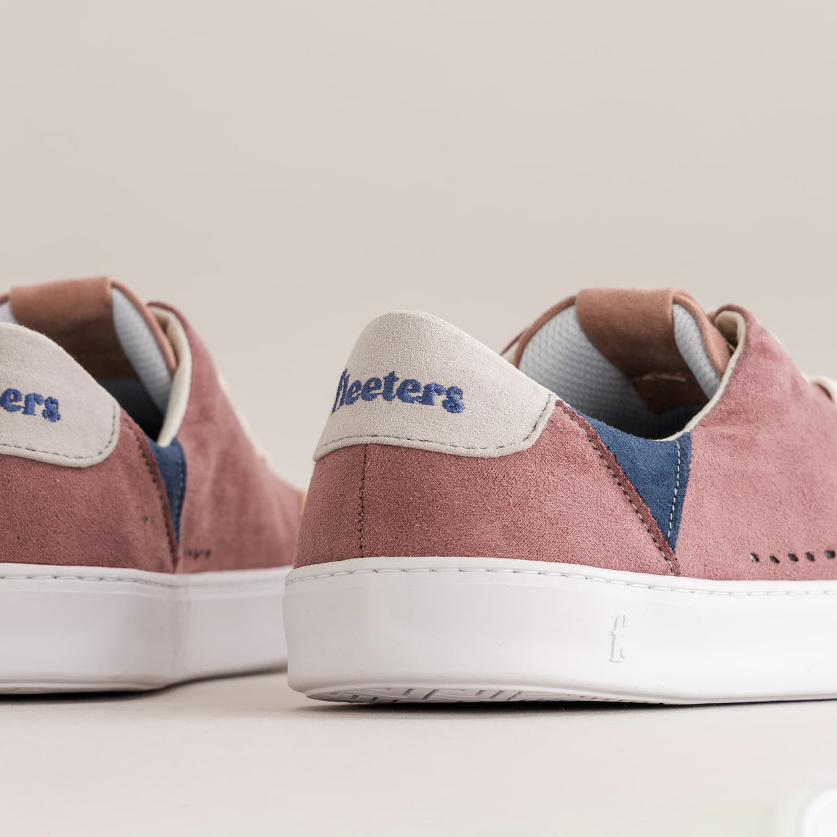 Close-up of a pair of suede barefoot sneakers showing the heel area, featuring dusty rose suede uppers, navy blue accents, white rubber soles, and a white heel tab with the brand name 'Fleeters' in blue.