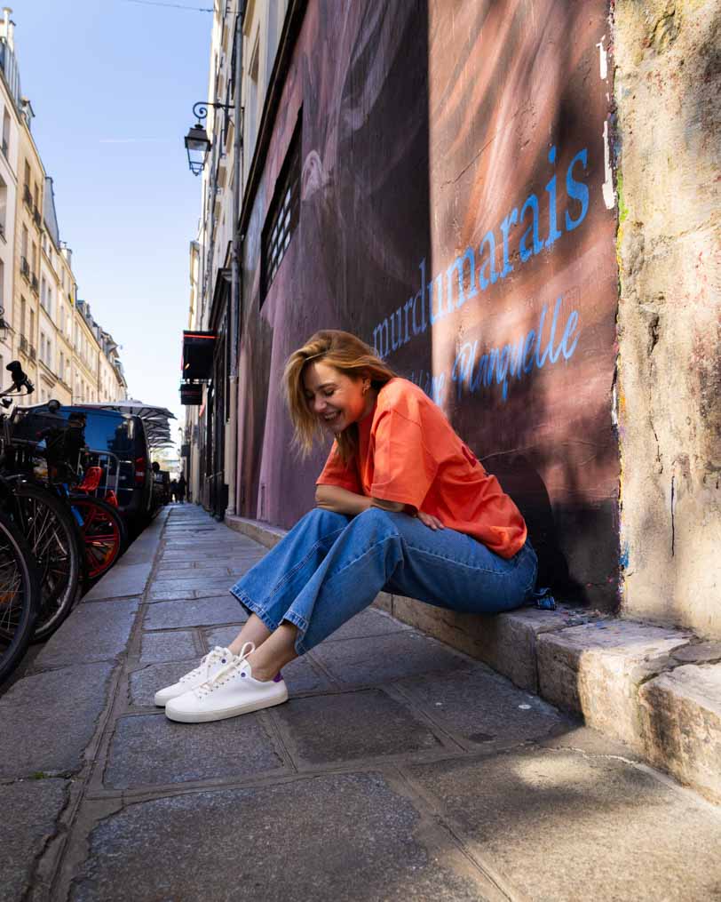 Person sitting on a stone ledge against a wall with a mural in an urban setting